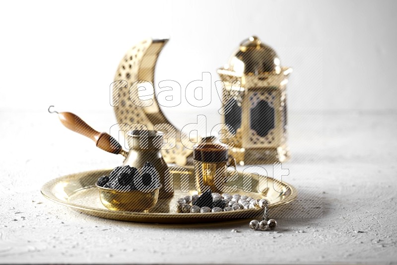 Dried plums in a metal bowl with coffee and prayer beads on a tray beside lanterns in a light setup