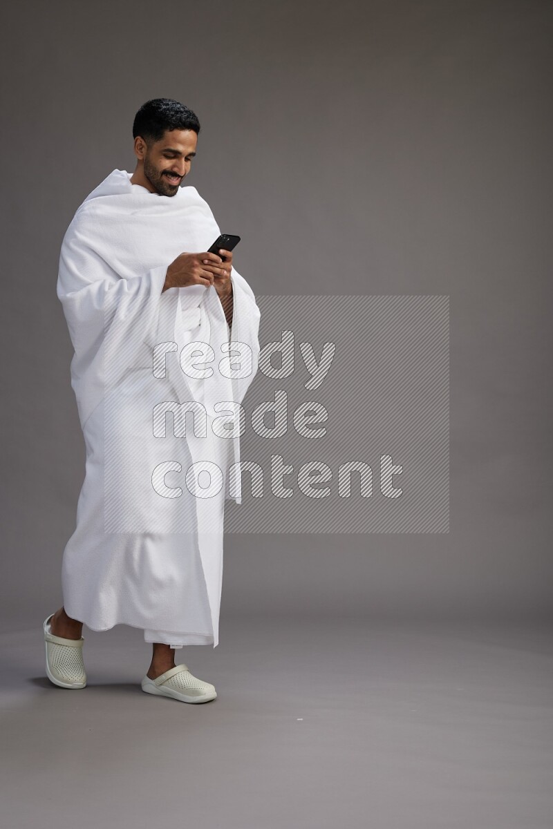 A man wearing Ehram Standing texting on phone on gray background
