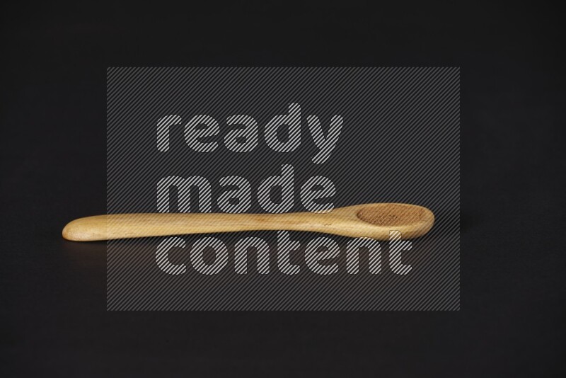 بودرة القرفة في ملعقة خشبية على خلفية سوداء