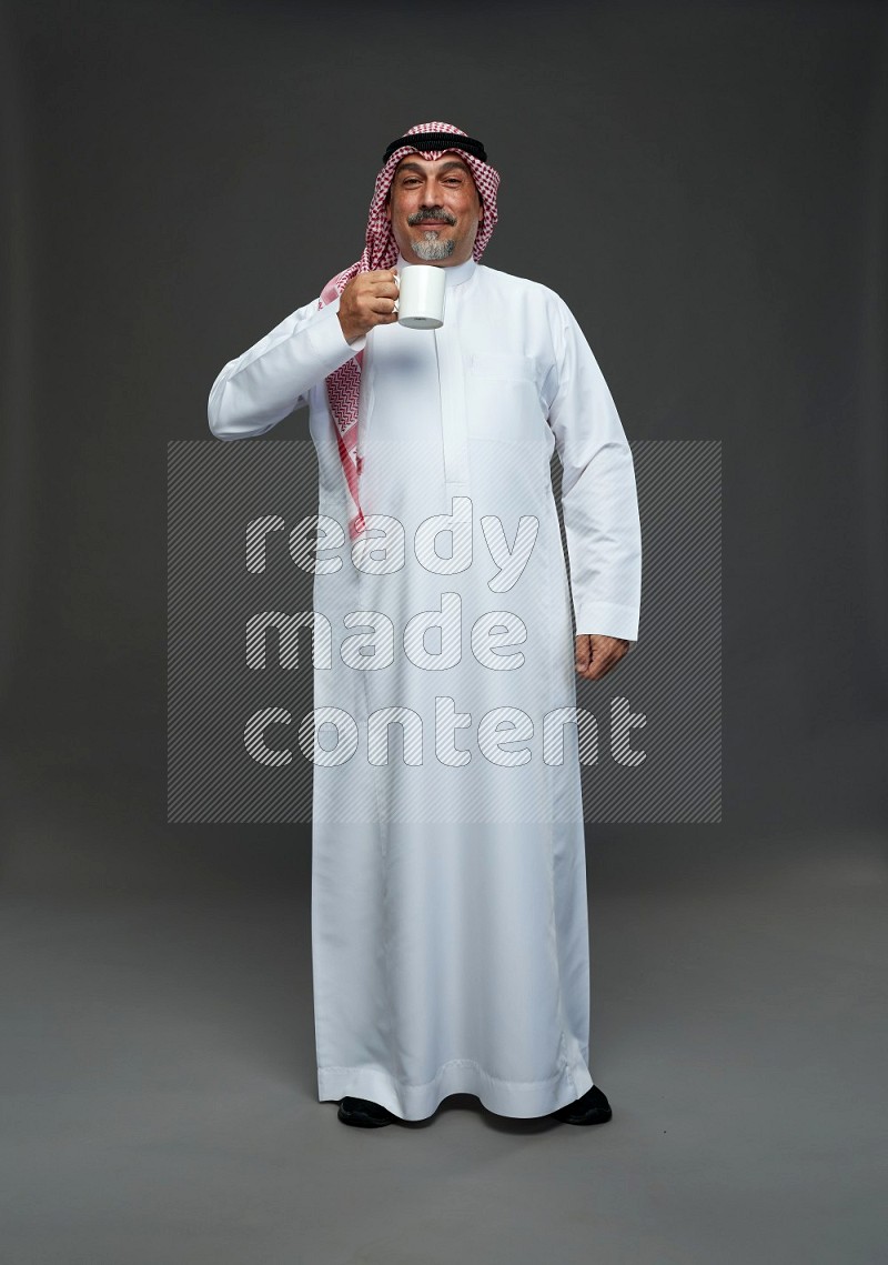 Saudi man with shomag Standing holding mug on gray background