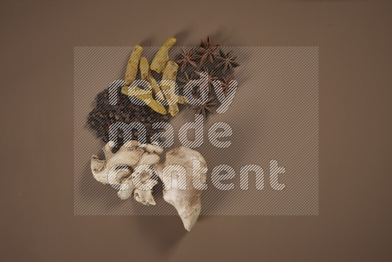 بهارات كاملة متنوعة تتضمن زنجبيل طازج ومجفف، أعواد قرفة، هيل، أصابع كركم، قرنفل، يانسون نجمي على خلفية بيج