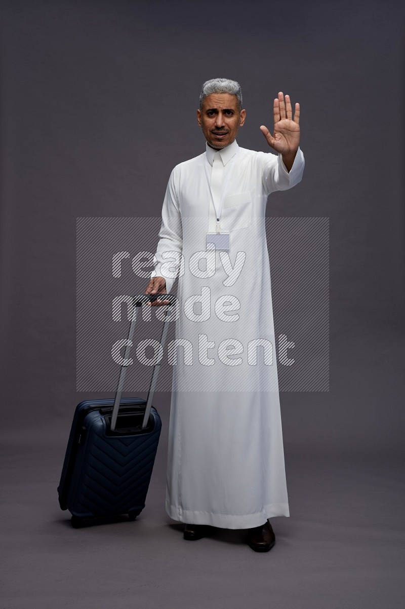 Saudi man wearing thob with neck strap employee badge standing holding bag on gray background