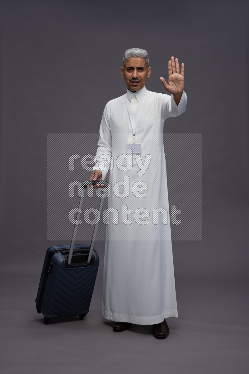 Saudi man wearing thob with neck strap employee badge standing holding bag on gray background