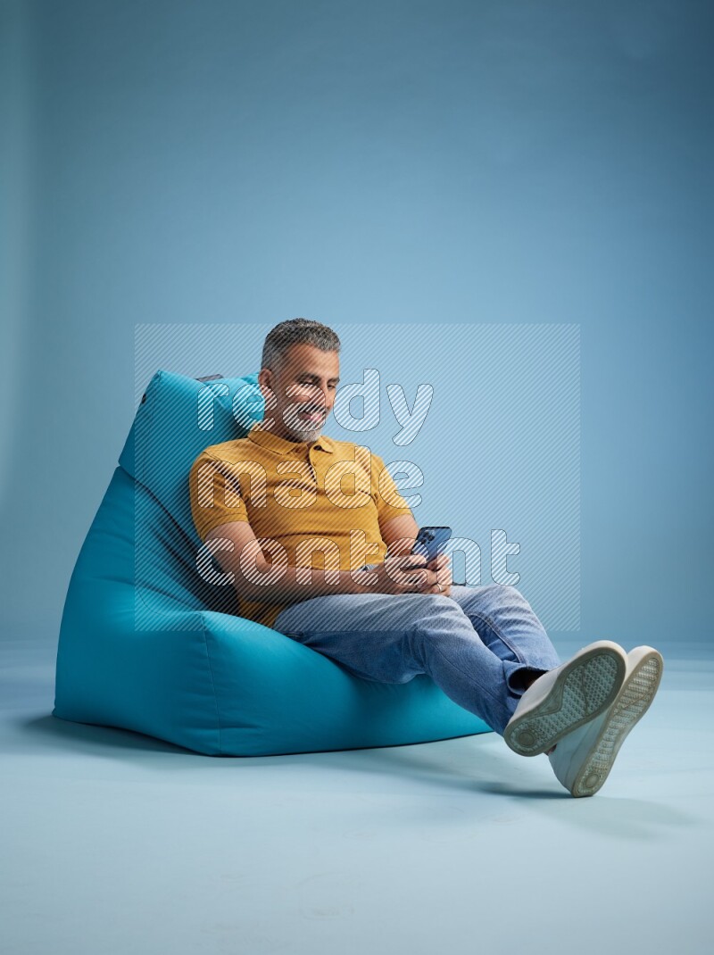 A man sitting on a blue beanbag and texting on phone