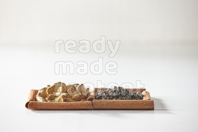 مربعان من أعواد القرفة ممتلئان بحبوب الفلفل الأسود وأصابع الكركم علي خلفية بيضاء