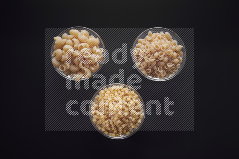 Different pasta types in glass bowls on black background