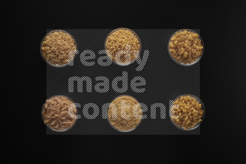 Different pasta types in 6 glass bowls on black background