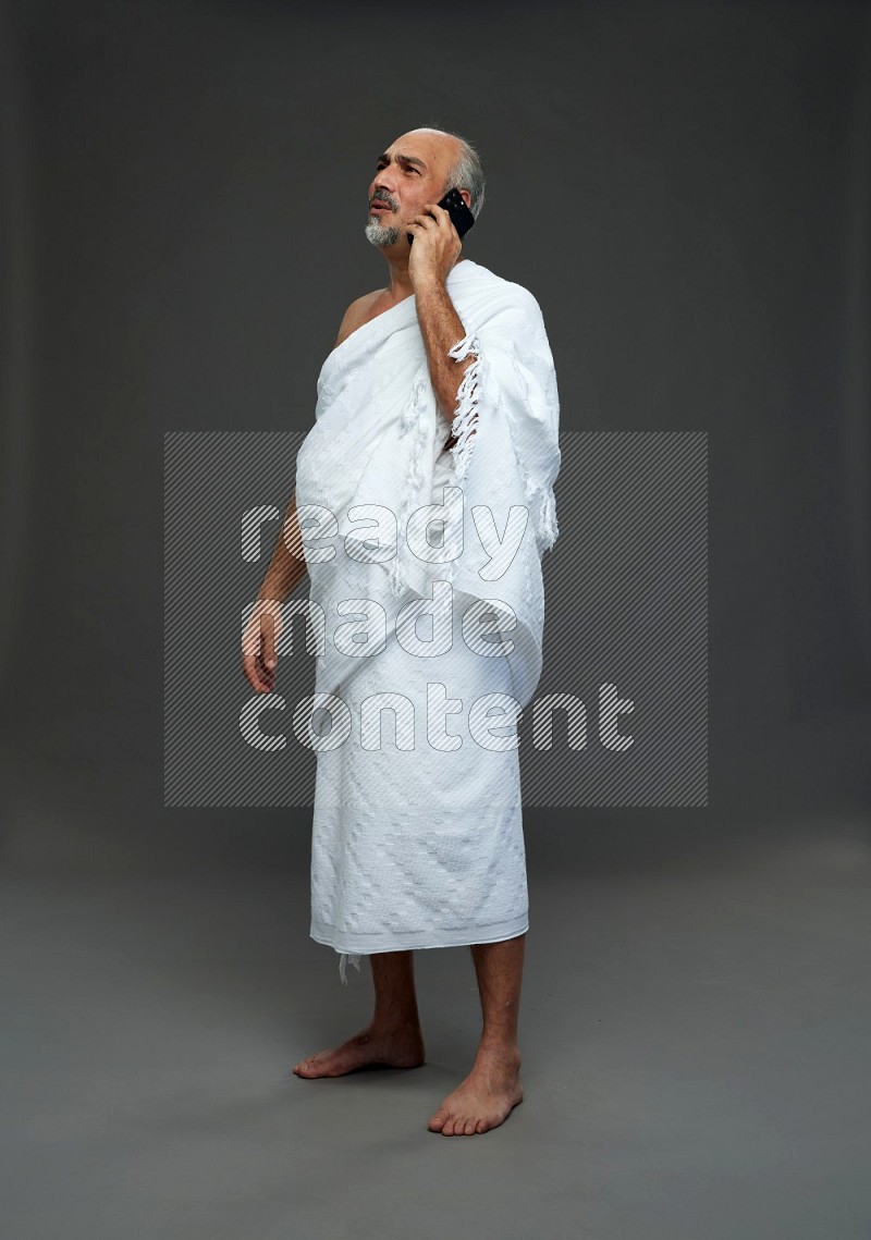 A man wearing Ehram Standing talking on phone on gray background