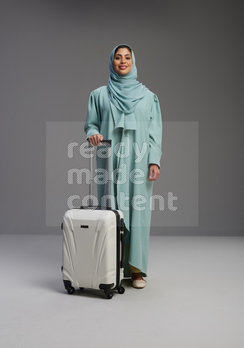Saudi Woman wearing Abaya standing holding Travel bag on Gray background