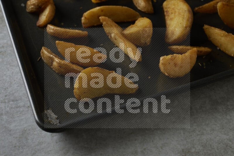 wedges potato in a black stainless steel rectangle tray on grey textured counter top
