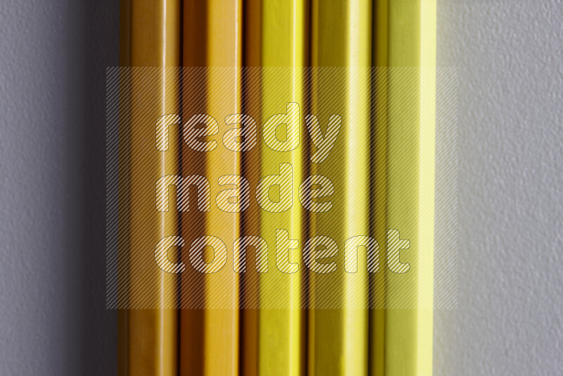 A collection of sharpened colored pencils arranged showcasing a gradient of yellow hues on grey background