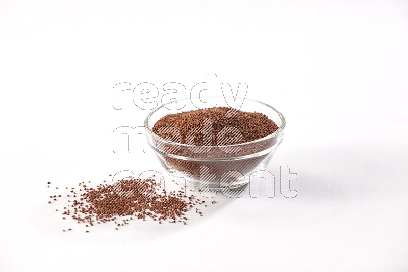 A glass bowl full of garden cress seeds with more seeds spread on a white flooring