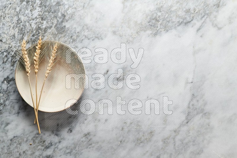 Wheat stalks on Multicolored Pottery Plate on grey marble flooring, Top view