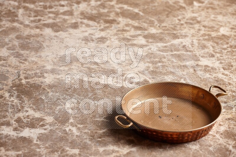 A small copper pan on beige marble background