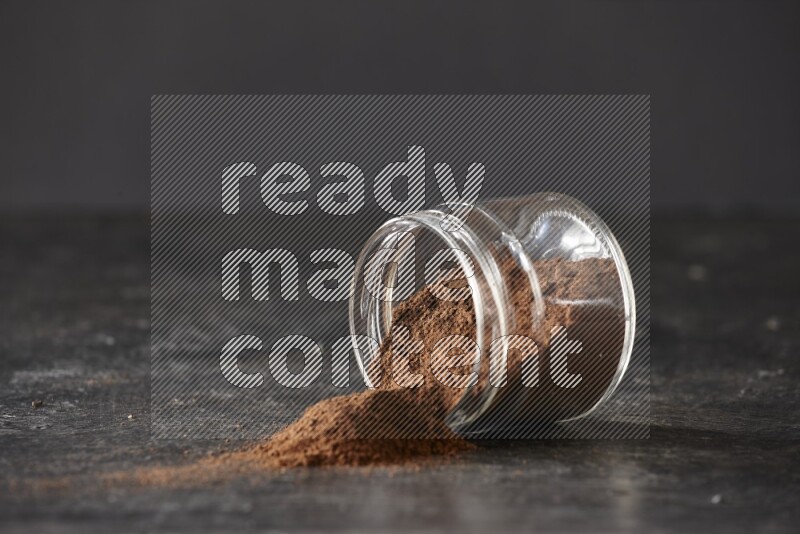 A flipped glass jar full of cloves powder on a textured black flooring