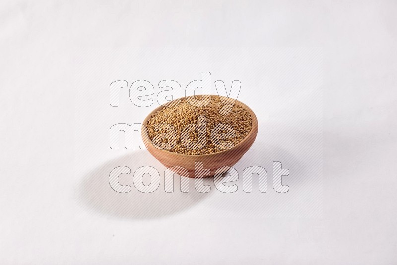 A wooden bowl full of mustard seeds on a white flooring