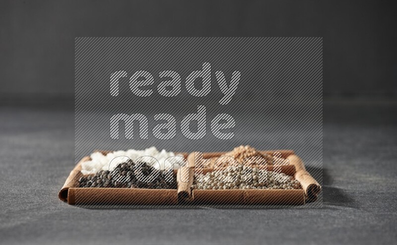 4 مربعات من عيدان القرفة ممتلئة بحبوب الفلفل الأسود والفلفل الأبيض والملح الأبيض وحبوب الخردل على أرضية سوداء