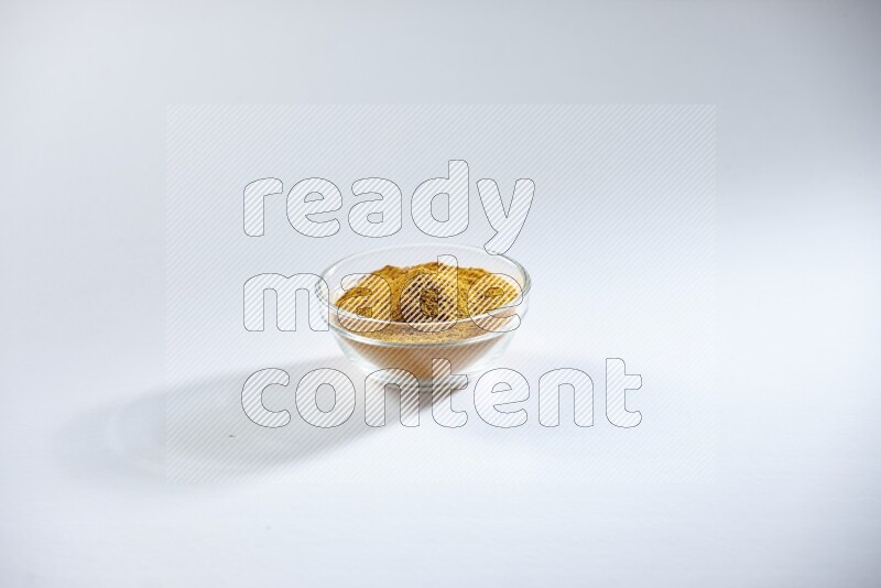 A glass bowl full of turmeric powder on white flooring