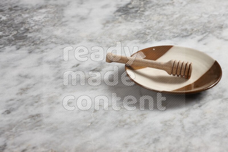 Multicolored pottery plate with wooden honey dipper in it on grey marble background