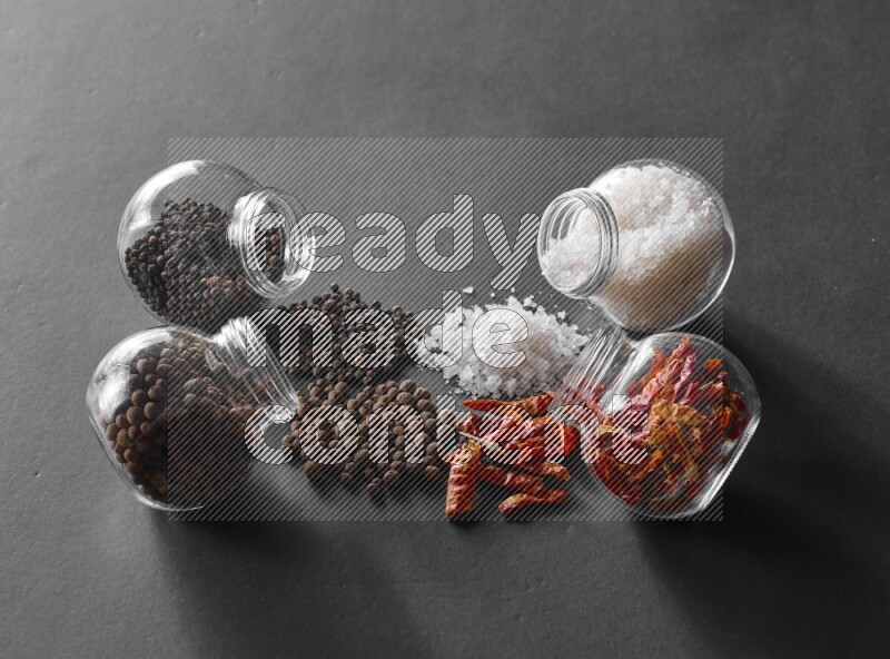 ملح وفلفل حار وفلفل أسود وحبوب الفلفل الحلو في أوعية زجاجية علي خلفية سوداء