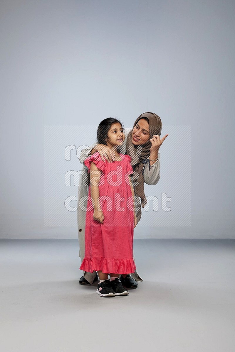 A girl and her mother interacting with the camera on gray background