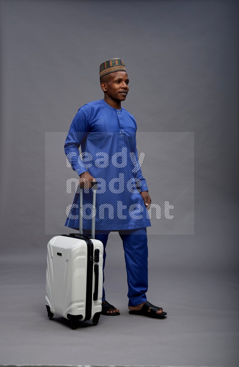 Man wearing Nigerian outfit standing holding bag on gray background