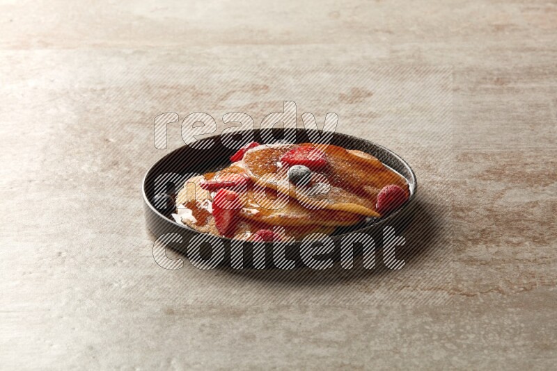 Three stacked mixed berries pancakes in a black plate on beige background
