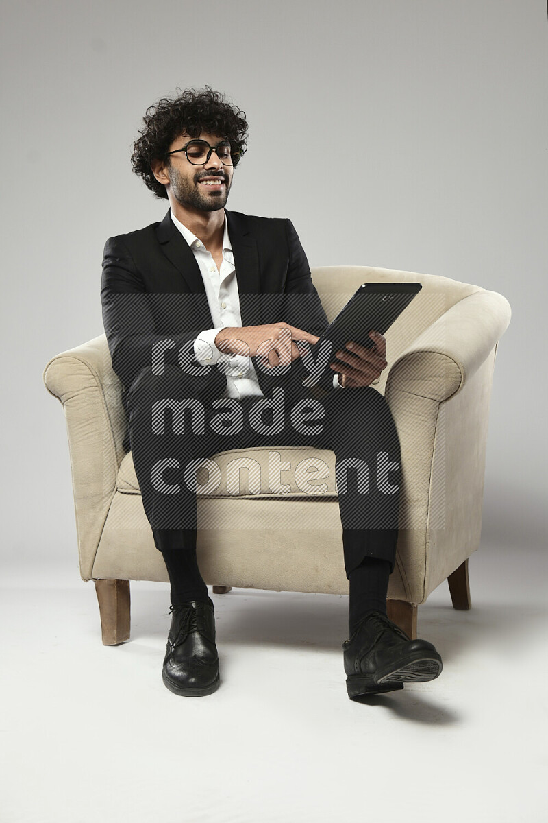 A man wearing formal sitting on a chair browsing on a tablet on white background