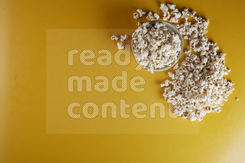 A white pottery bowl full of popcorn with popcorn beside it on a yellow background in different angles
