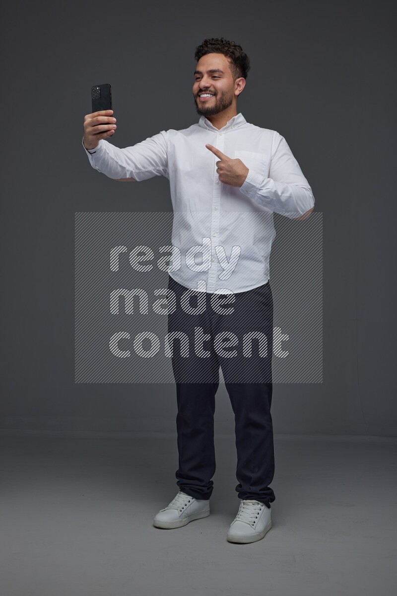 A man wearing smart casual and taking selfie with his phone eye level on a gray background