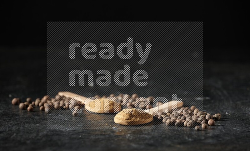 ملاعق خشبية ممتلئة ببودرة بهار الفلفل الحلو وحبوبه بجانبها على خلفية سوداء