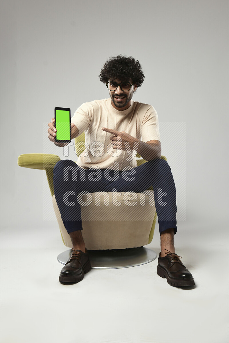 رجل يرتدي ملابس كاجوال يجلس علي كرسي و يحمل هاتف علي خلفية بيضاء