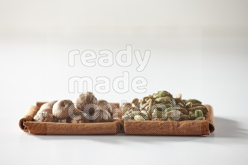 مربعان من أعواد القرفة ممتلئان بحبوب الهيل وجوزة الطيب علي خلفية بيضاء