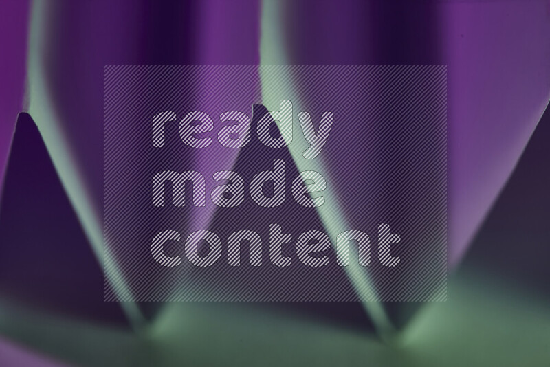 A close-up abstract image showing sharp geometric paper folds in green and purple gradients