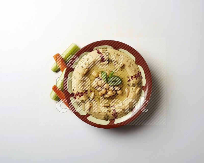 Hummus in a traditional plate garnished with zaatar & sumak on a white background