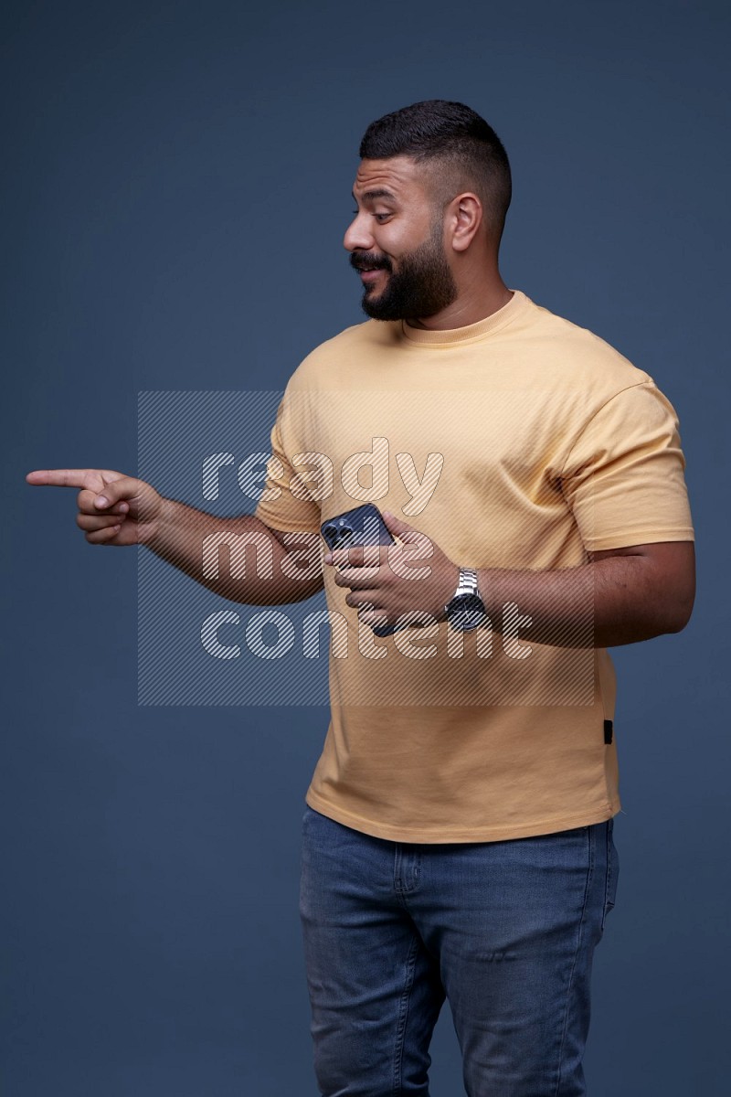 A man Pointing at a Smartphone on Blue Background wearing Orange T-shirt