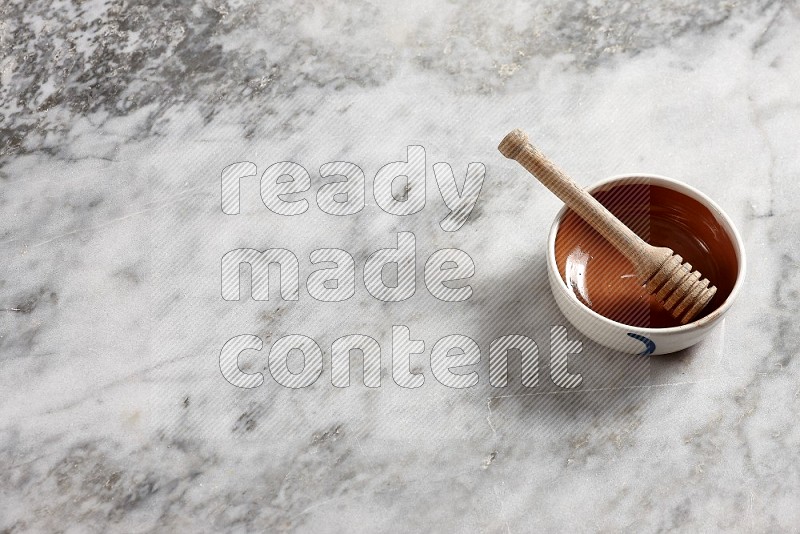 Multicolored Pottery bowl with wooden honey handle in it, on grey marble flooring, 65 degree angle