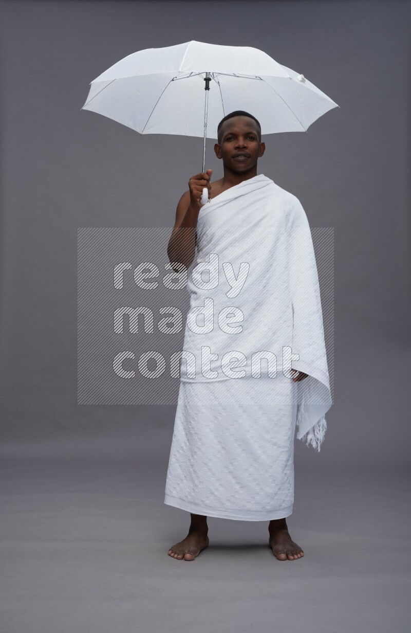 A man wearing Ehram Standing holding umbrella on gray background