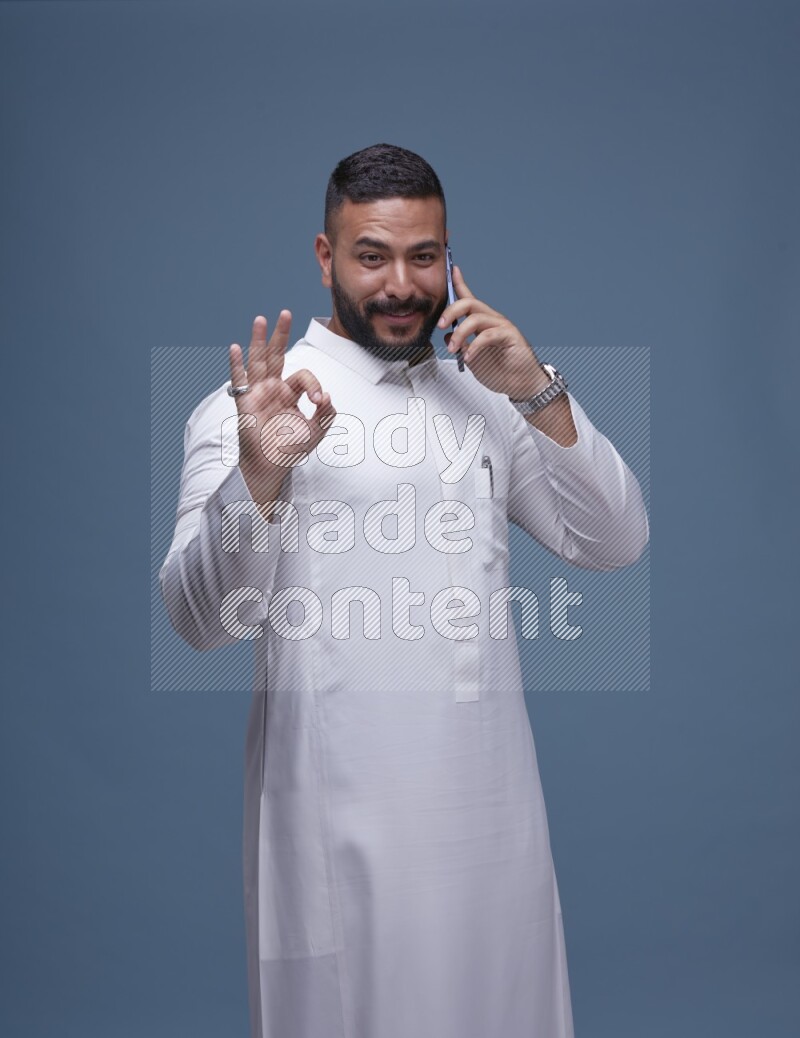 A Saudi man calling on blue background wearing Saudi Thob
