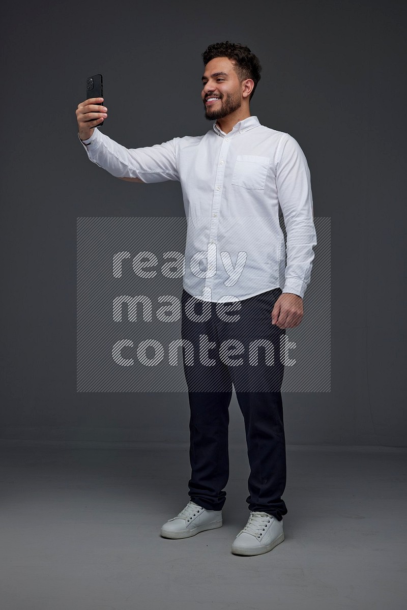 A man wearing smart casual and taking selfie with his phone eye level on a gray background