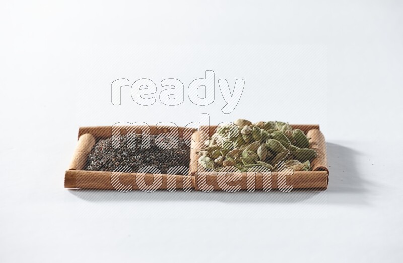 مربعان من أعواد القرفة ممتلئان بالشاي الأسود وحبوب الهال علي خلفية بيضاء