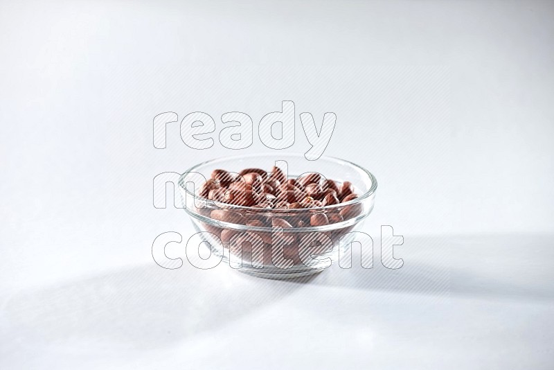 A glass bowl full of red skin peanuts on a white background in different angles