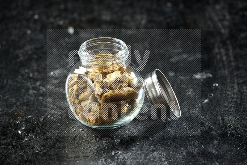 A glass spice jar full of dried turmeric whole fingers on a textured black flooring