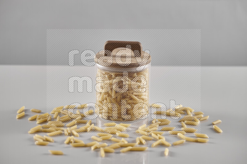 Raw pasta in a glass jar on light grey background