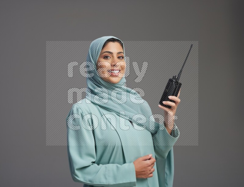 Saudi Woman wearing Abaya standing holding walkie-talkie on Gray background