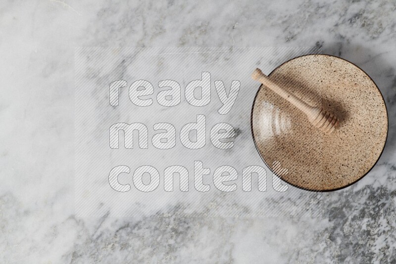 Multicolored pottery plate with wooden honey dipper in it on grey marble background