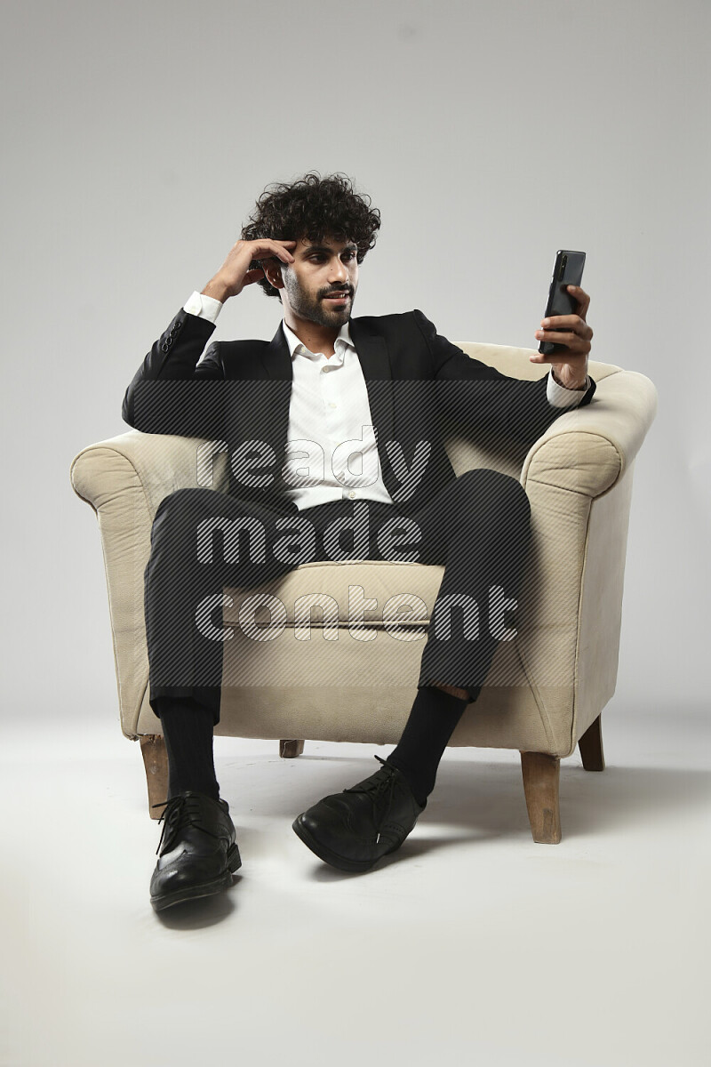 A man wearing formal sitting on a chair browsing on the phone on white background