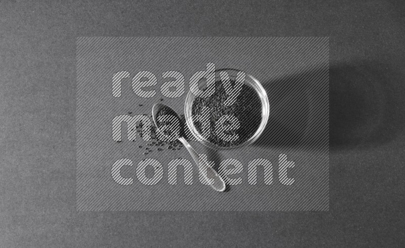 وعاء زجاجي ممتلئ ببذور حبة البركة مع ملعقة معدنية مليئة بحبة البركة علي خلفية سوداء