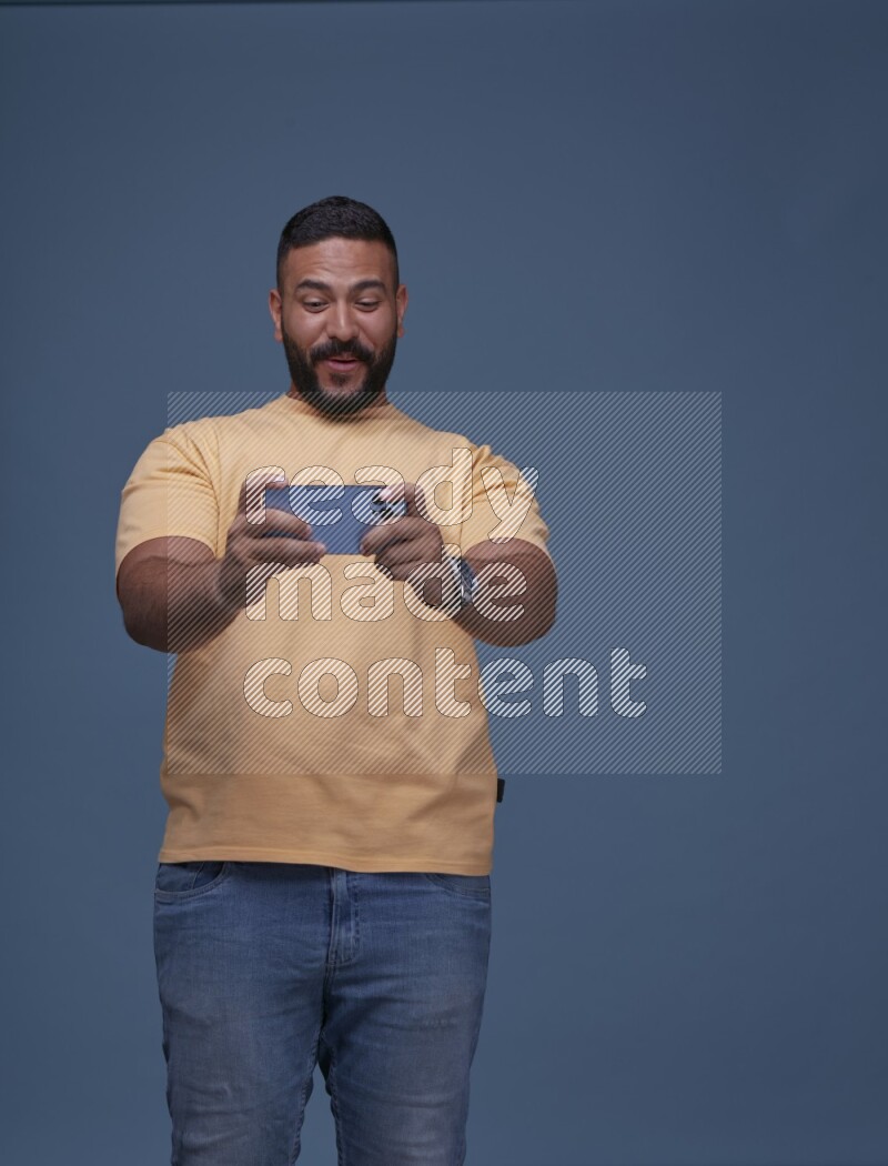 رجل يرتدي بنطال ازرق جينز وقميص اصفر بأكمام قصيره يلعب في جواله