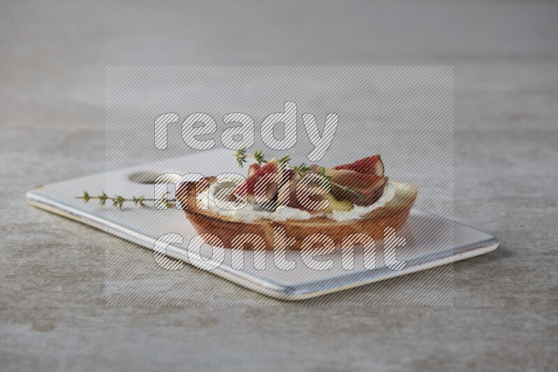 quarters of figs with cream cheese on toasted sourdough slice on a wooden board on textured grey background